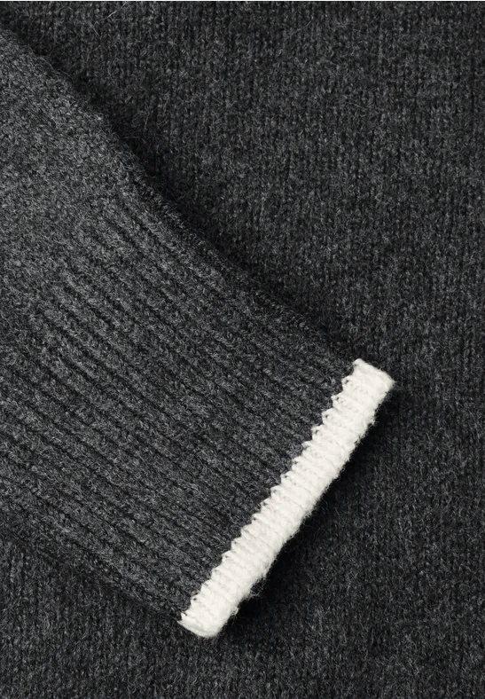Nahaufnahme eines dunkelgrauen Strickpullovers mit geripptem Ärmelbündchen und weißem Rand.