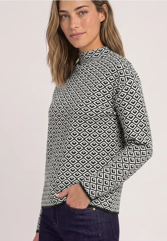 Frau mit schwarz-weißem Rautenmuster-Pullover, lässig mit einer Hand in der Hosentasche.