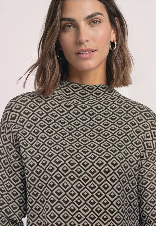 Frau mit schulterlangem, dunklem Haar trägt Pullover mit geometrischem Rautenmuster.