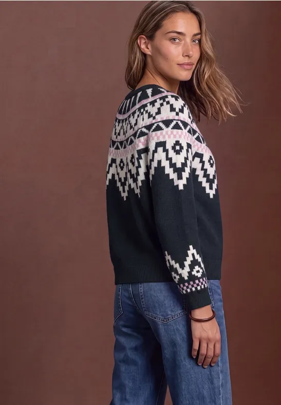 Frau mit modischem Norweger-Pullover in Schwarz mit weißem Muster und Jeans, seitlich gewandt.