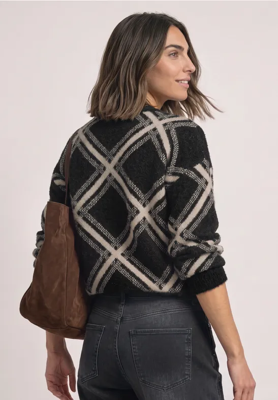 Frau steht seitlich in schwarz-weißem Pullover, dunkle Jeans, trägt eine braune Tasche über der Schulter.