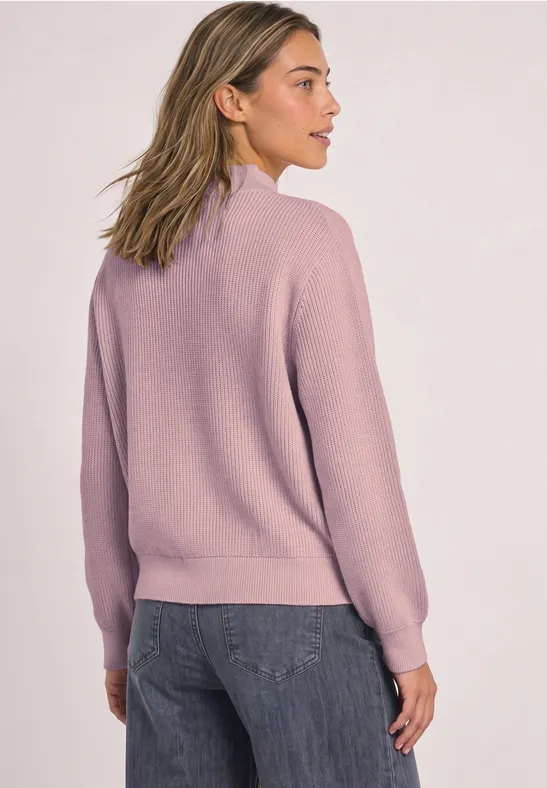 Eine Frau von hinten in einem fliederfarbenen Pullover und Jeans.