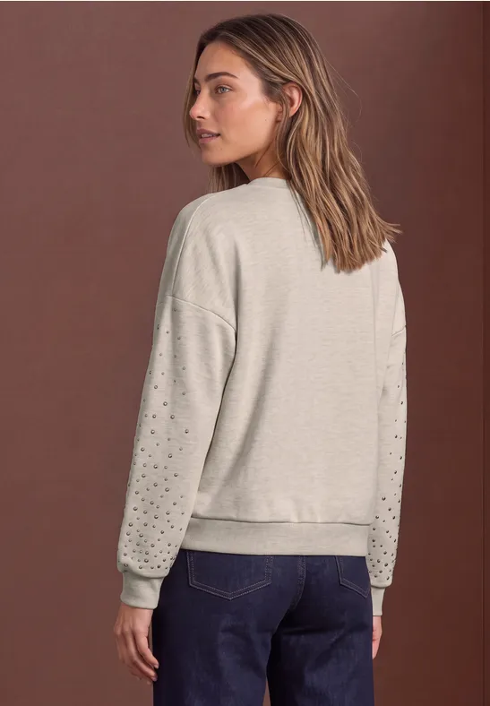 Vue arrière d'une femme en sweat gris clair à motifs ajourés aux manches et jean bleu, fond marron.