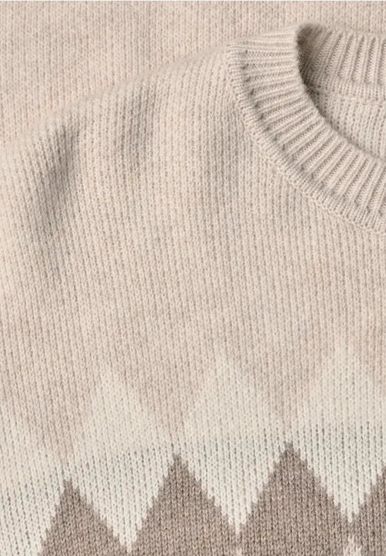 Nahaufnahme eines gestrickten Pullovers mit Rautenmuster in Beige und Weiß.