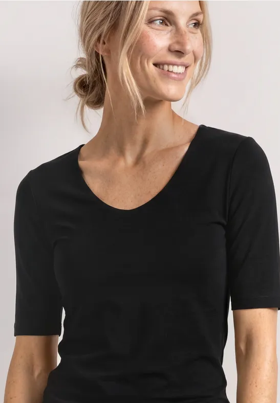 Vrouw met blond haar in een knot, draagt een zwart T-shirt met halflange mouwen tegen een witte achtergrond.