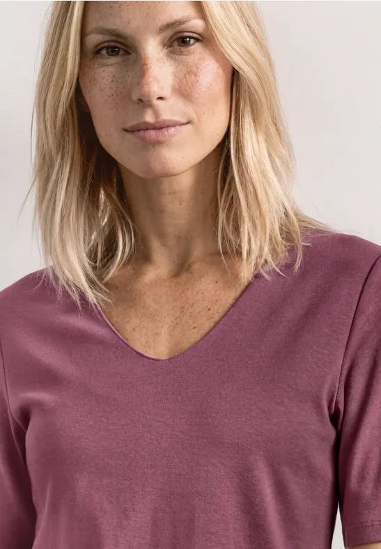 Porträt einer Frau mit langen blonden Haaren, Sommersprossen, dezentem Make-up und V-Ausschnitt-Pullover in Mauve.