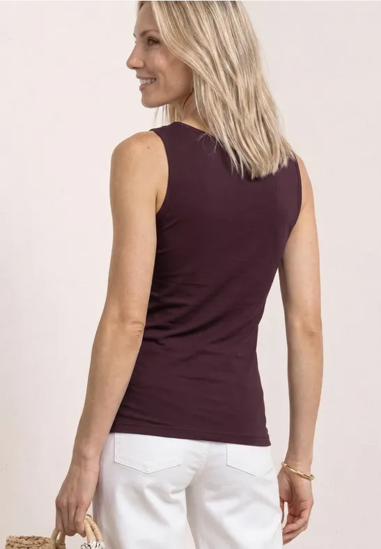 Vrouw van achteren met blond haar, bordeaux top en witte broek.