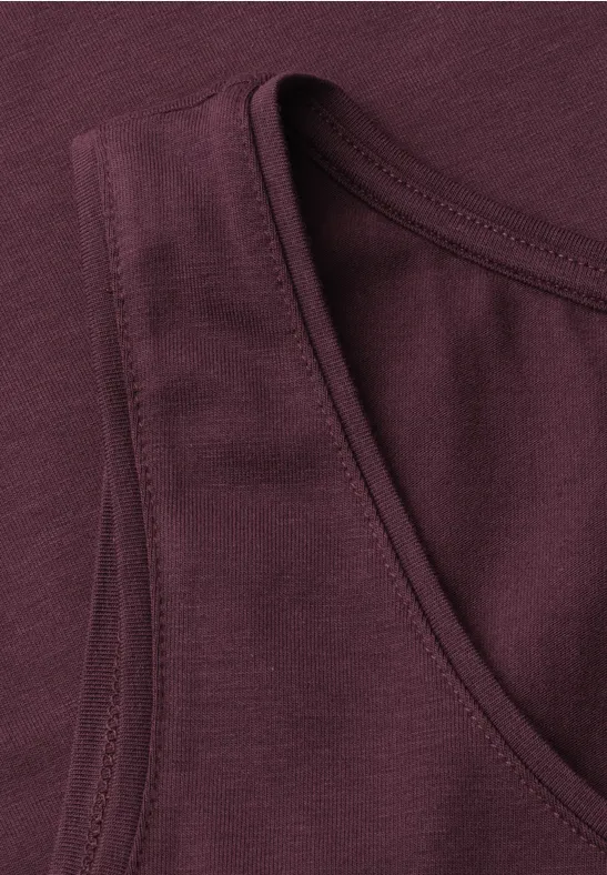 Close-up van een bordeauxkleurige mouwloze tanktop met zichtbare naden bij de halslijn.