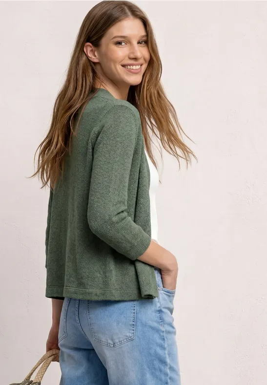 Femme vue de profil portant un gilet vert, un top blanc et un jean.