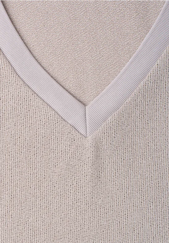 Close-up van een beige gebreide trui met V-hals.