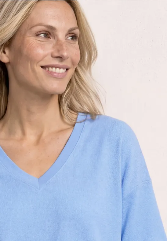 Vrouw met blond haar in een lichtblauw V-hals shirt tegen een lichte achtergrond.