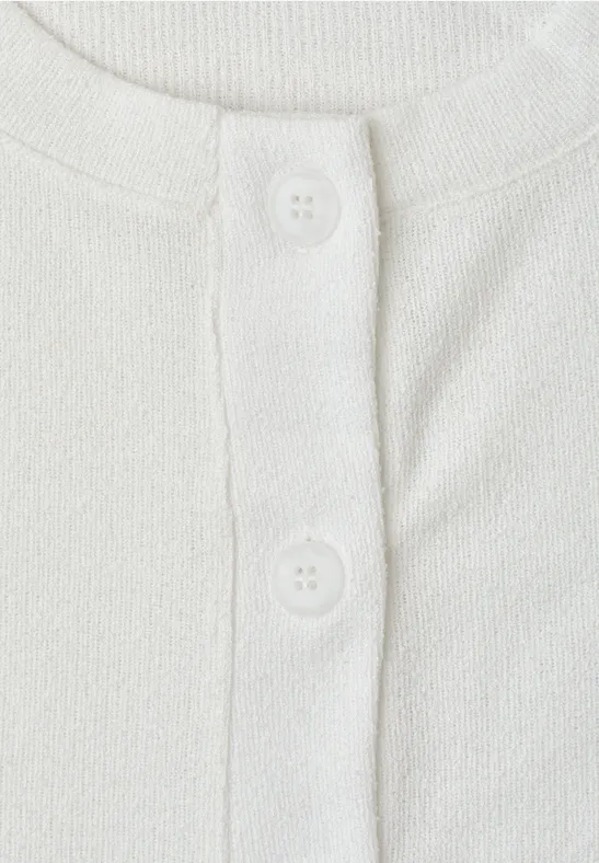 Nahaufnahme eines weißen T-Shirts mit Knopfleiste und zwei weißen Knöpfen.