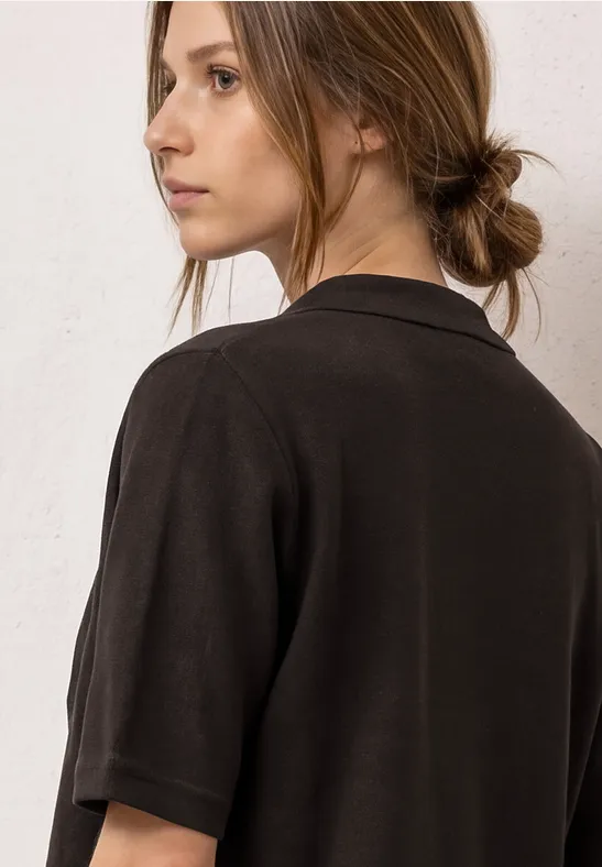 Jeune femme aux cheveux attachés porte un t-shirt noir à manches courtes et regarde de côté.