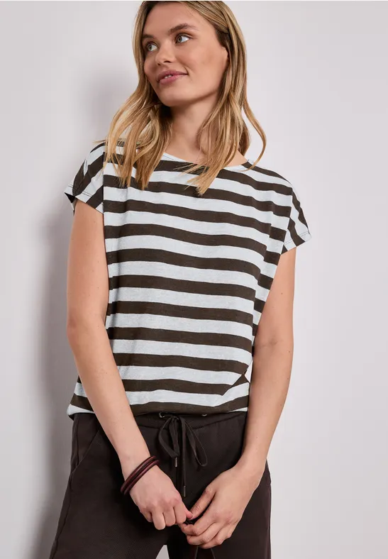 Femme portant un t-shirt rayé noir et blanc et un pantalon noir devant un fond neutre.