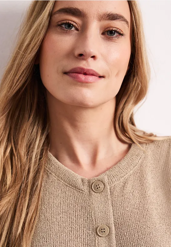 Een persoon met lang haar draagt een beige gebreide trui met knopen.