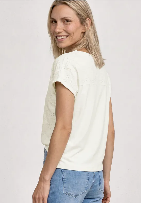 Vrouw van achteren in wit T-shirt en blauwe spijkerbroek, schouderlang blond haar, effen achtergrond.