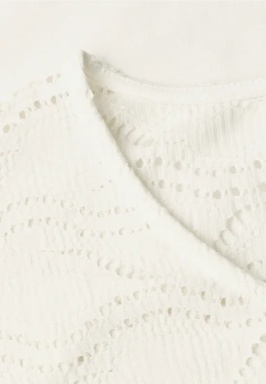 Close-up van een crèmekleurig gehaakt topje met V-hals en golvend patroon.