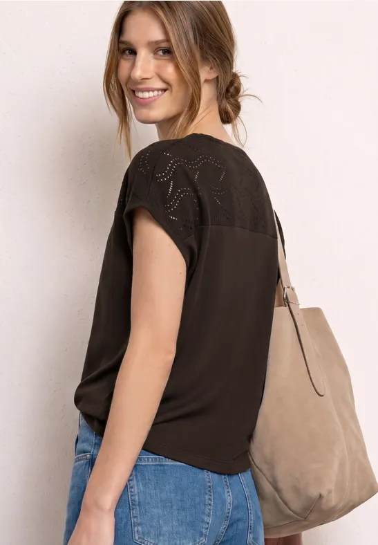 Vrouw in een zwart topje met kant, blauwe jeans en een grote beige tas over de schouder, zijaanzicht.