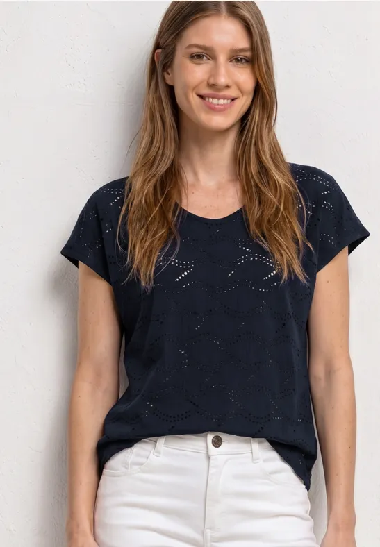Vrouw met lang haar draagt donkerblauw t-shirt en witte jeans voor lichte achtergrond.