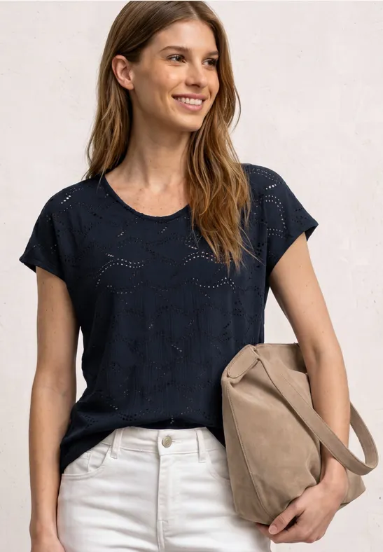 Vrouw in donkerblauw gebreid shirt, witte broek en draagt een beige tas.