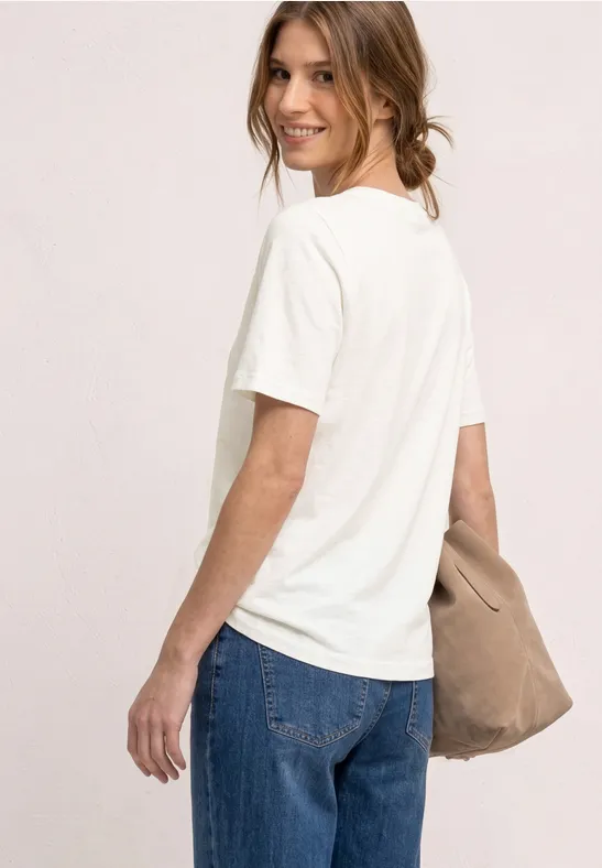 Een persoon van achteren draagt een wit T-shirt, een blauwe jeans en een beige tas.