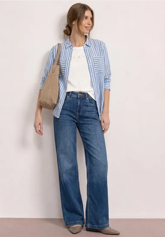 Vrouw met wit T-shirt, blauw gestreept overhemd, wijde jeans en beige schoudertas
