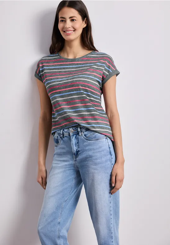 Vrouw in gestreept T-shirt en blauwe spijkerbroek tegen neutrale achtergrond.