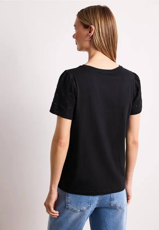 Achteraanzicht van een vrouw in een zwart T-shirt met korte mouwen en een lichtblauwe jeans tegen een witte achtergrond.