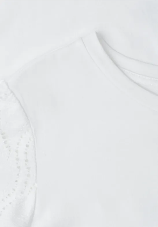 Close-up van een wit kindert-shirt met fijne kanten mouwtjes.