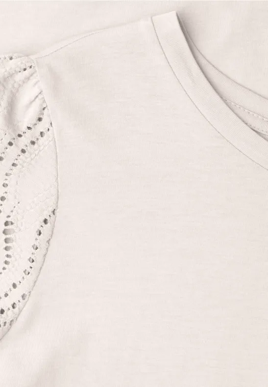 Hellbeiges T-Shirt mit Rundhalsausschnitt und mit funkelnden Nieten verzierten Ärmeln.