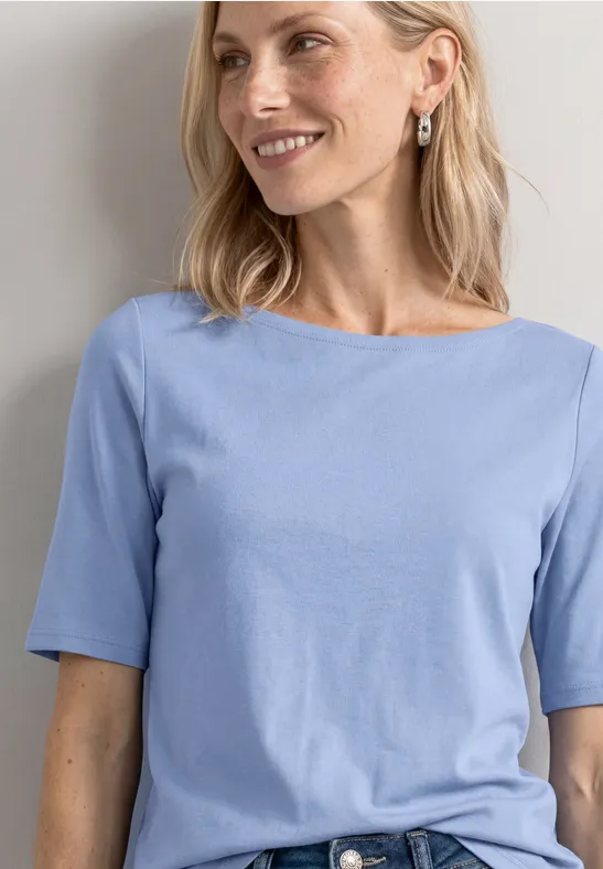 Een glimlachende vrouw met halflang blond haar draagt een lichtblauw T-shirt met korte mouwen.