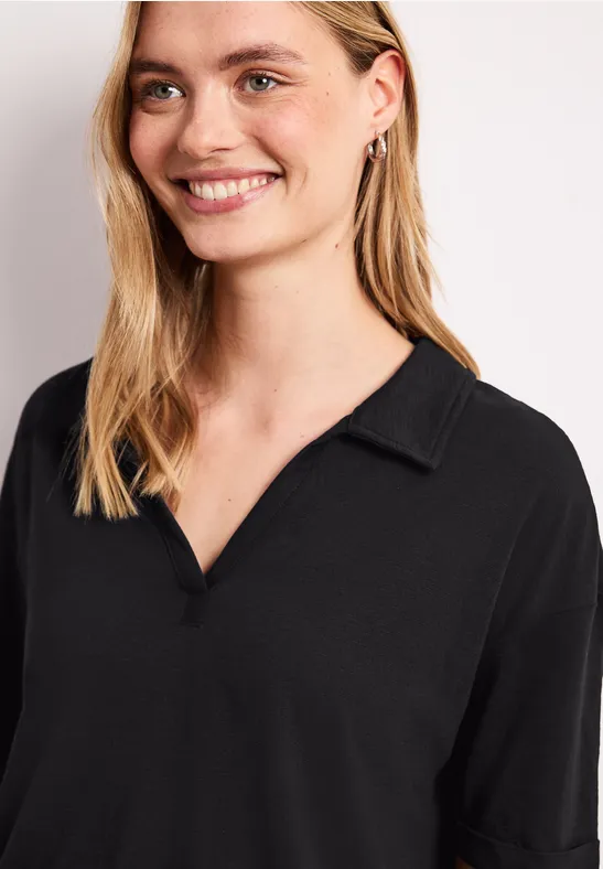 Glimlachende blonde vrouw in een zwart overhemd met V-hals en kraag voor een lichte achtergrond.