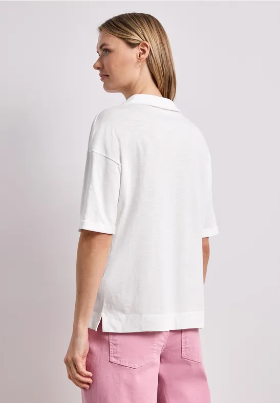 Vrouw van achteren in een los wit kortarmig poloshirt met kraag en een roze broek.