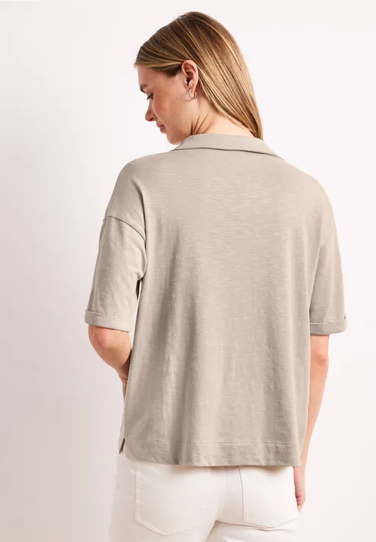 Vrouw van achteren in een beige T-shirt met korte mouwen en een witte spijkerbroek.