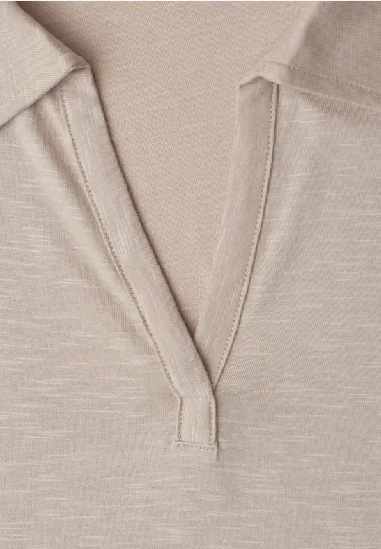 Close-up van een beige top met V-hals van lichtgewicht stof en zichtbare stiknaad.