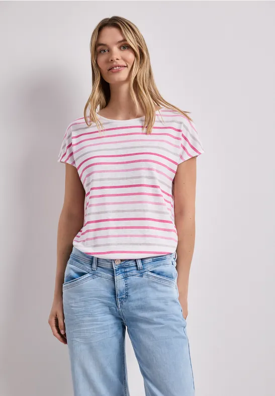 Vrouw in wit t-shirt met roze strepen en blauwe jeans voor een neutrale achtergrond.