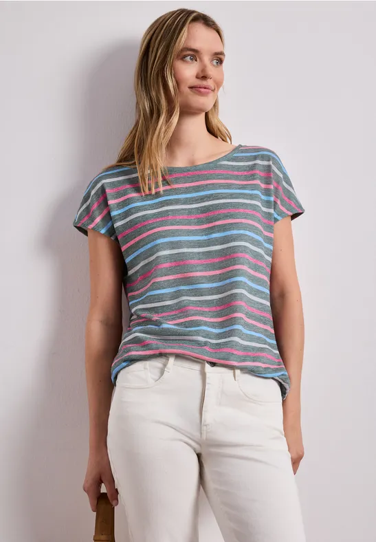 Persoon draagt gekleurd gestreept shirt en lichte broek voor een neutrale muur.