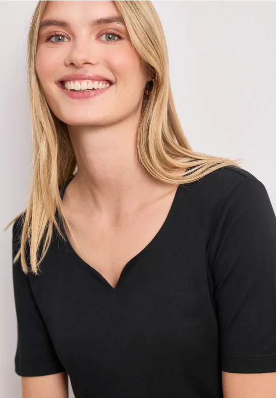 Frau mit langen blonden Haaren trägt ein schlichtes schwarzes Shirt mit V-Ausschnitt.