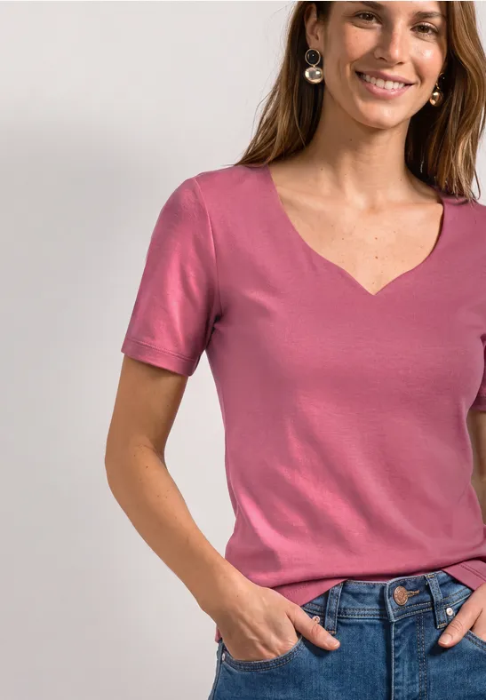Lächelnde Frau mit rosa T-Shirt und Jeans, Hände in den Taschen.