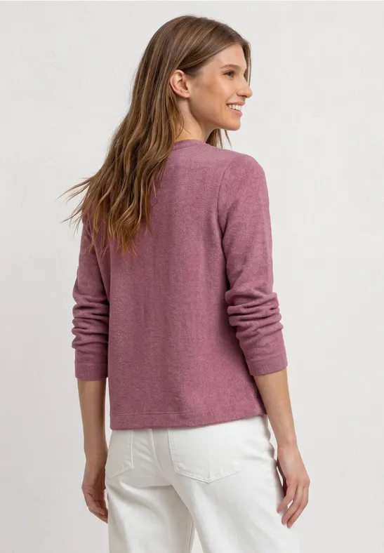Jeune femme de dos portant un pull rose et un pantalon blanc sur un fond clair.