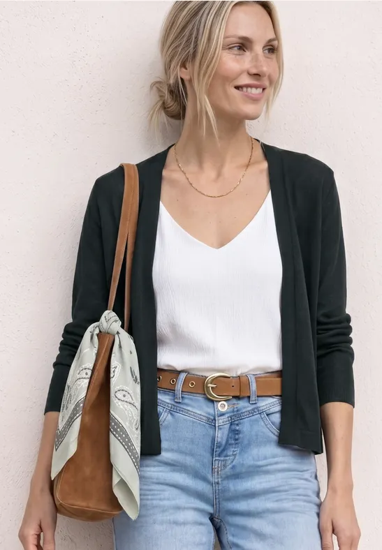 Femme en tenue décontractée avec gilet noir, débardeur blanc, jean, ceinture marron et sac à bandoulière avec foulard.