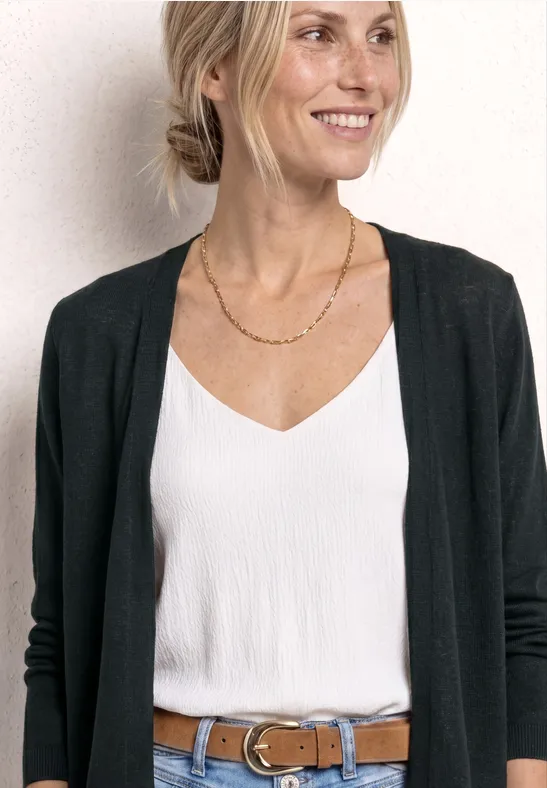 Personne portant un top blanc à décolleté V, gilet noir, ceinture marron et jean sur fond clair.