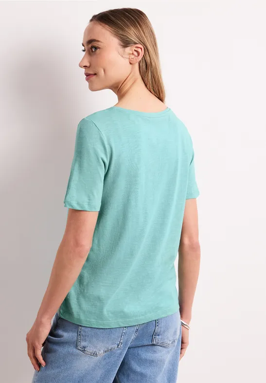 Vrouw van achteren in een turquoise t-shirt en spijkerbroek.