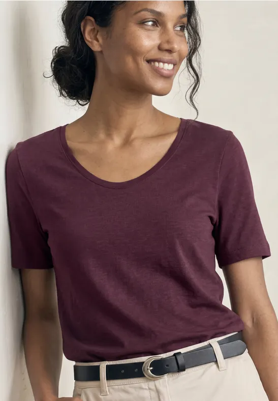 Lächelnde Frau in burgunderrotem T-Shirt mit kurzen Ärmeln und schwarzem Gürtel.