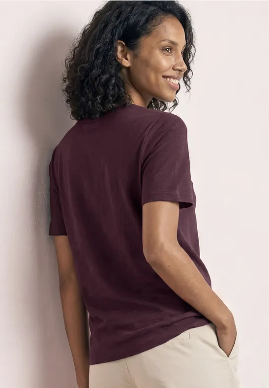 Person von hinten in bordeauxrotem T-Shirt und hellen Hosen