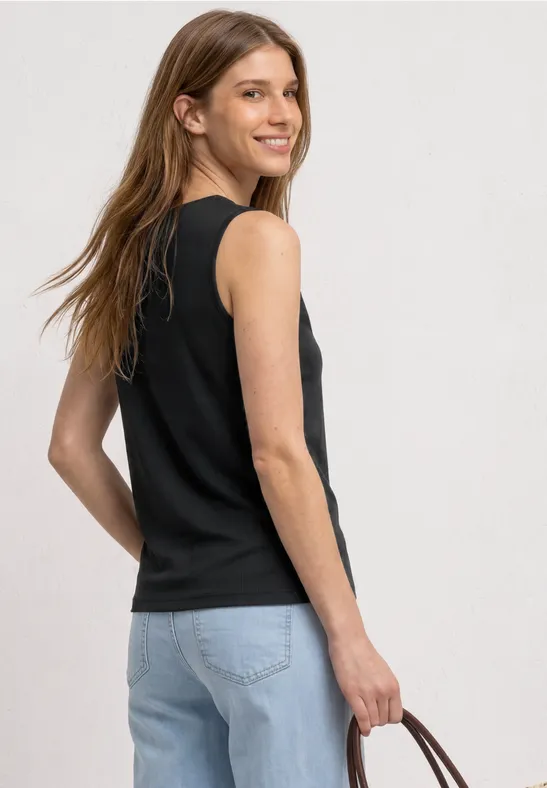 Vrouw in halfprofiel met een zwart mouwloos topje, blauwe jeans en een bruine handtas.