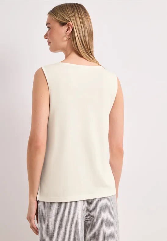 Vrouw van achteren in een mouwloos crèmekleurig topje en grijze broek.