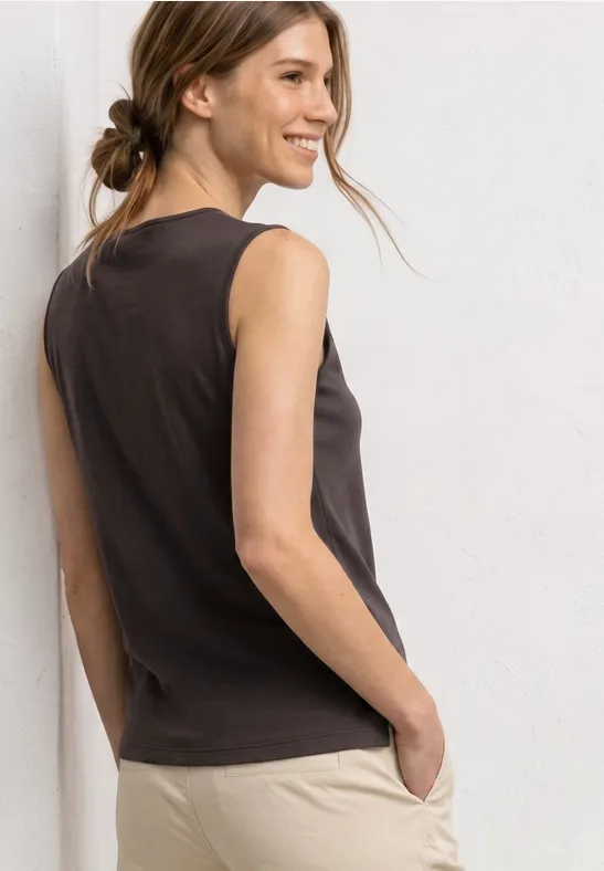 Vrouw van achteren in een donkergrijs mouwloos topje en beige broek, haar los gestoken in een nonchalante knot.