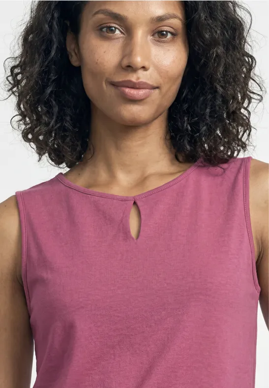 Vrouw met krullend haar, draagt roze mouwloos hemd tegen een witte achtergrond.