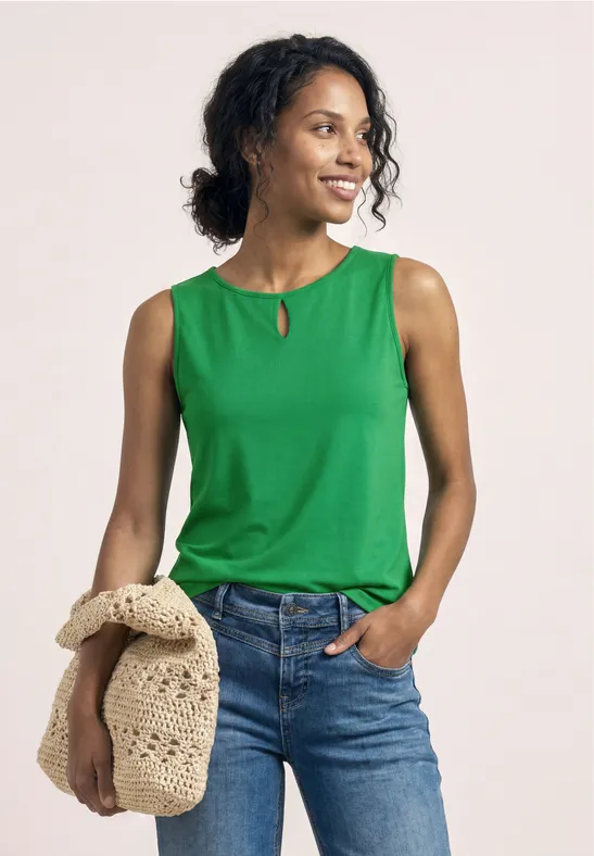 Vrouw in groen mouwloos topje en jeans met een beige gehaakte tas.